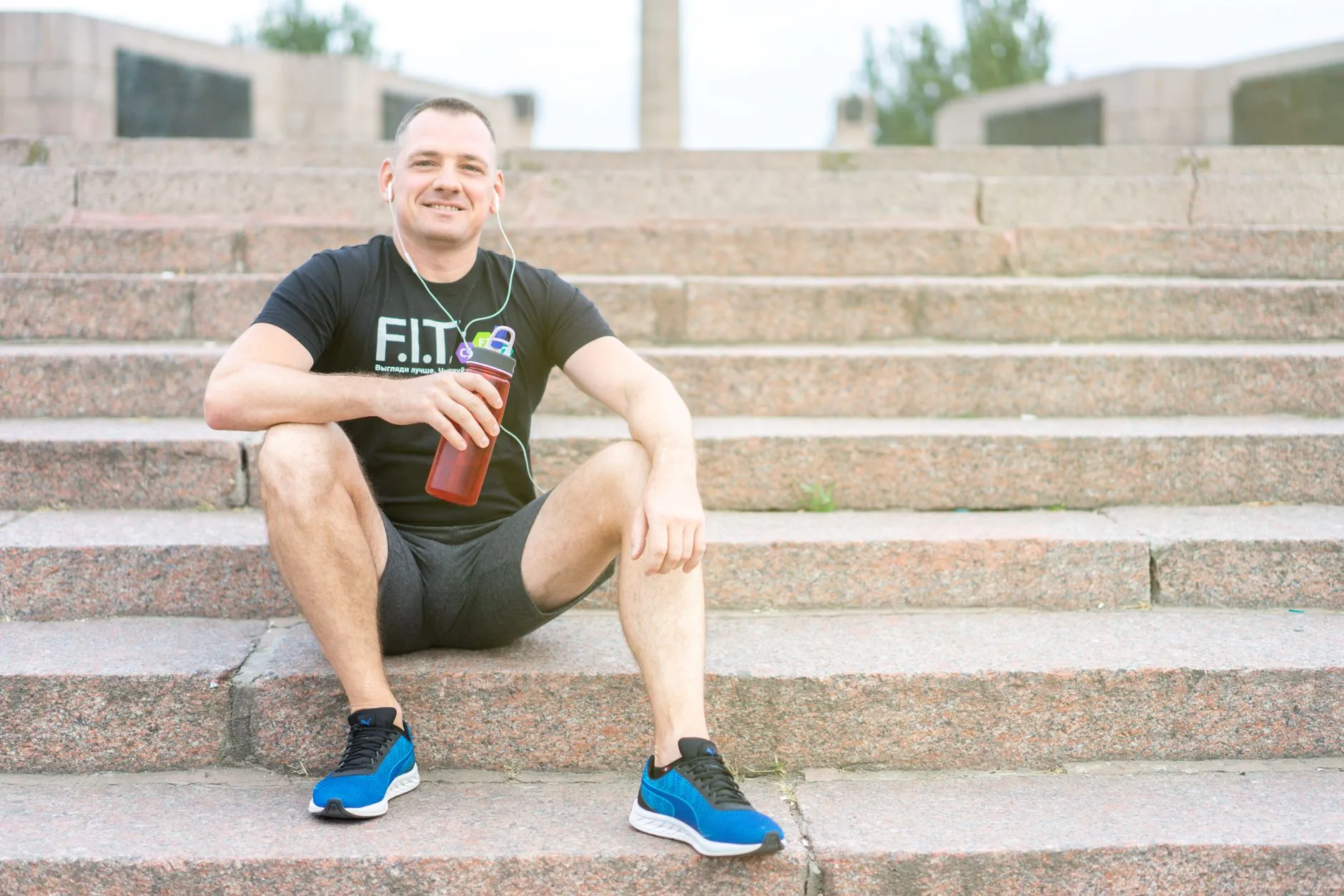 A fit, smiling man resting on stone steps after an outdoor workout