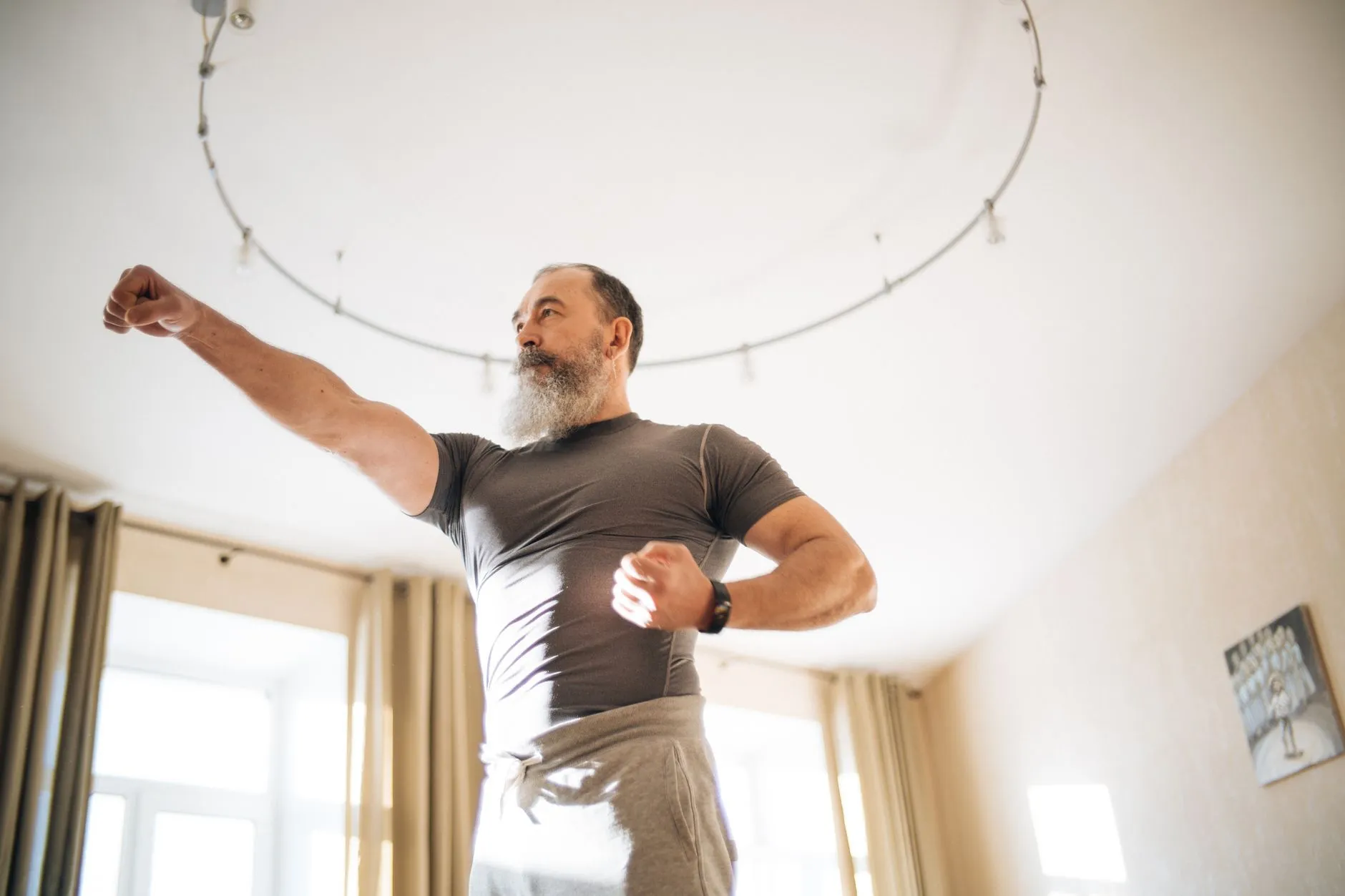 A fit, grey-bearded man training in a bright room