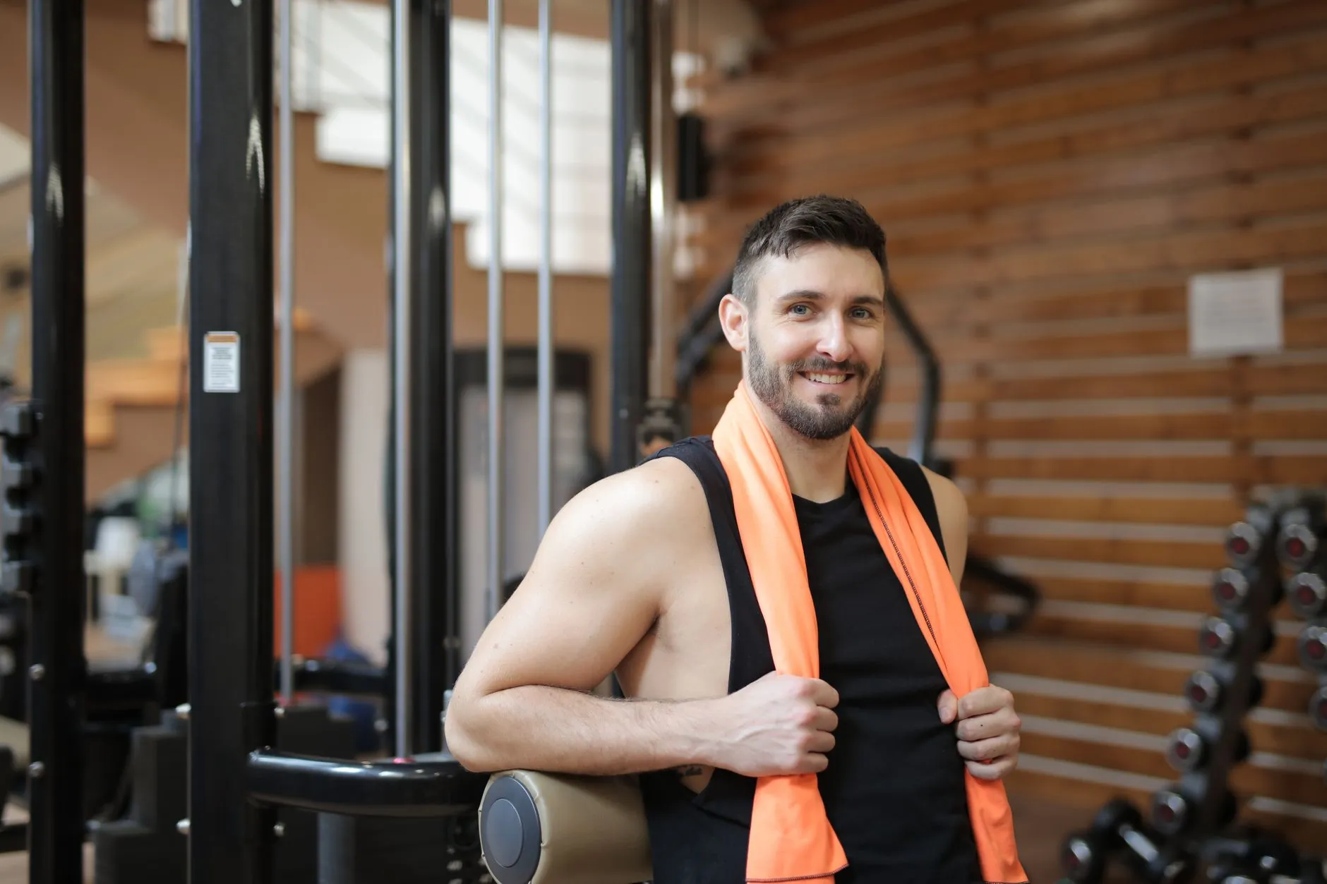 A fit, smiling man with a towel over his shoulder in a bright gym