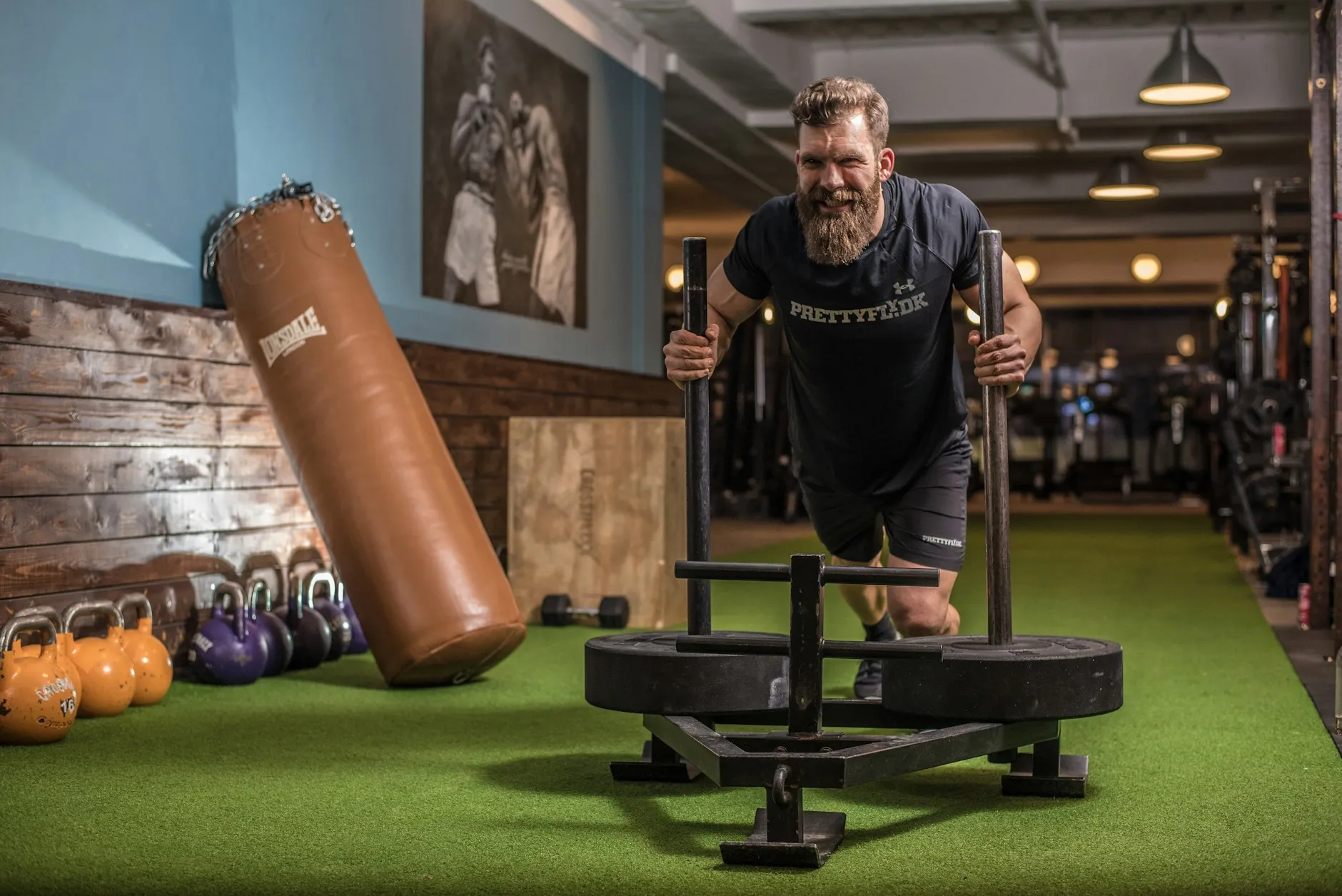 A bearded man driving a weighted sled across the gym floor